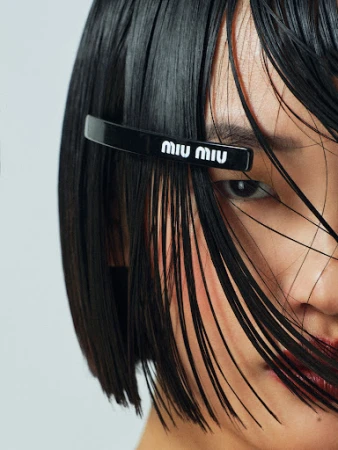 Close-up shot of a woman with short black hair and a black hair clip with the brand name Miu Miu in white letters.
