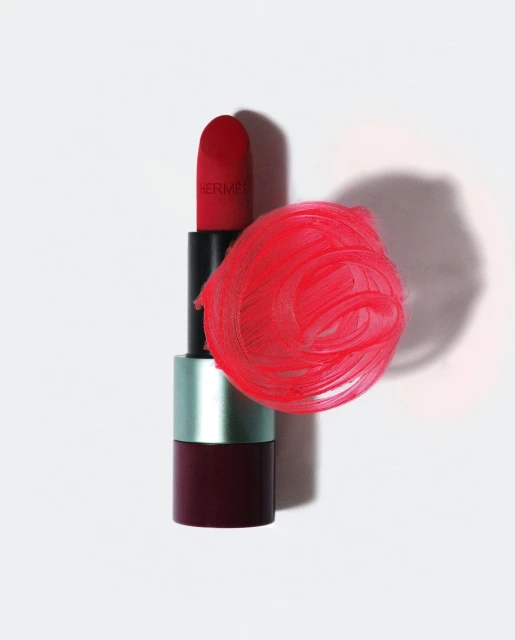 Still life studio shot of a red Hermes lipstick with a smear of red lipstick on a clean white surface. Beauty product photography.