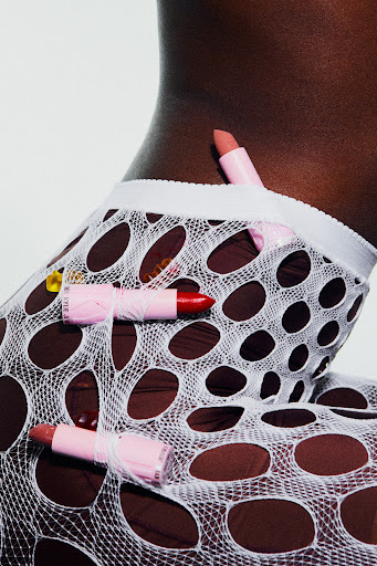 Close-up shot of a dark-skinned person wearing a white, net-like garment with pink lipsticks attached by thread against a white background.