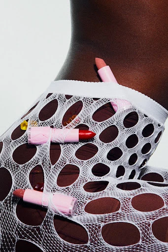 Close-up shot of a dark-skinned person wearing a white, net-like garment with pink lipsticks attached by thread against a white background.