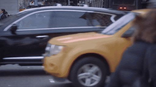 Urban scene capturing a yellow taxi and a black SUV in motion on a city street, with a blurry figure in the foreground.