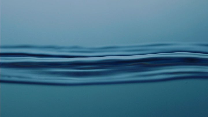 Abstract image of calm water surface with gentle waves, captured in shades of deep and light blue, creating a serene aquatic scene.