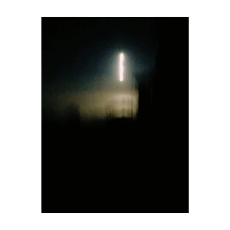 Abstract, blurred photograph of a vertical white light source on a dark background with a dark, indistinct structure in front.
