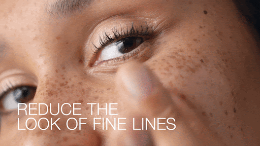 Close-up of a tan-skinned adult female with freckles touching the skin under her eye, with text overlay 'Reduce the Look of Fine Lines'.