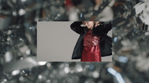 Smiling woman in a sequin dress and jacket dancing against a neutral background with shimmering bokeh-style foreground and background.