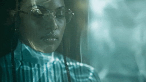 Close-up of a woman wearing glasses and a striped shirt against a blurry blue background with bokeh, capturing a contemplative mood.