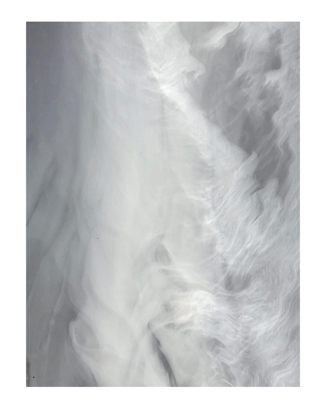 Abstract background with swirling patterns and shades of gray, white, and silver creating a dynamic, fluid-like texture in a square format.