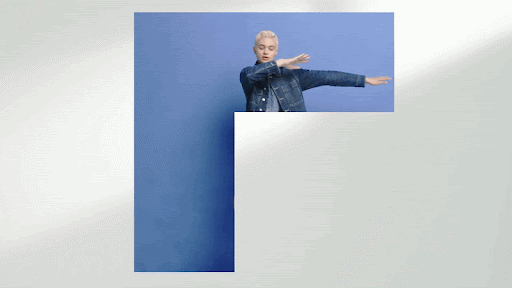 Short-haired person wearing a denim jacket framing arms outward against a blue cutout block and white background.