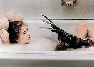 A young adult woman is taking a bath with a clawed glove resting on her head, lit by artificial light in an indoor setting.