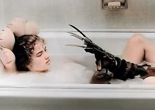 A young adult woman is taking a bath with a clawed glove resting on her head, lit by artificial light in an indoor setting.