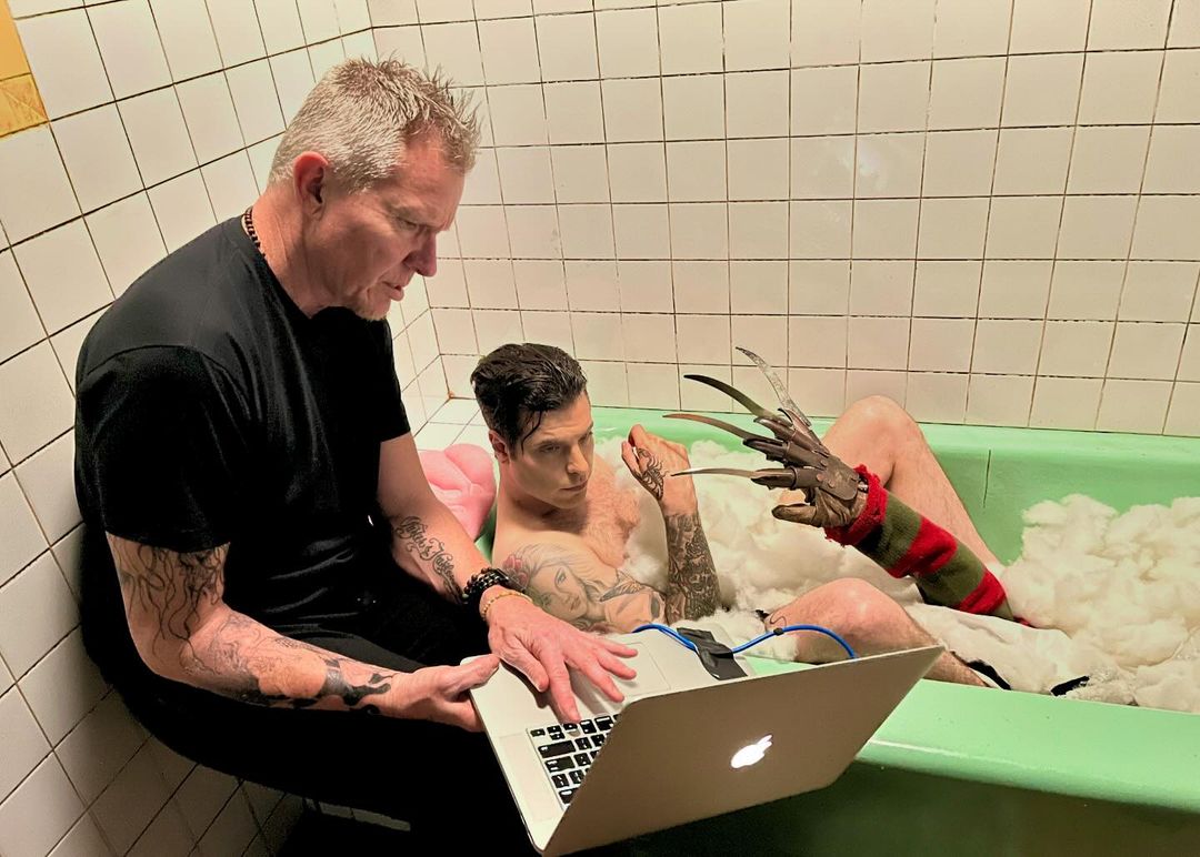 Behind-the-scenes of a shoot with two men: one operates a laptop while the other in a bathtub with clawed glove.