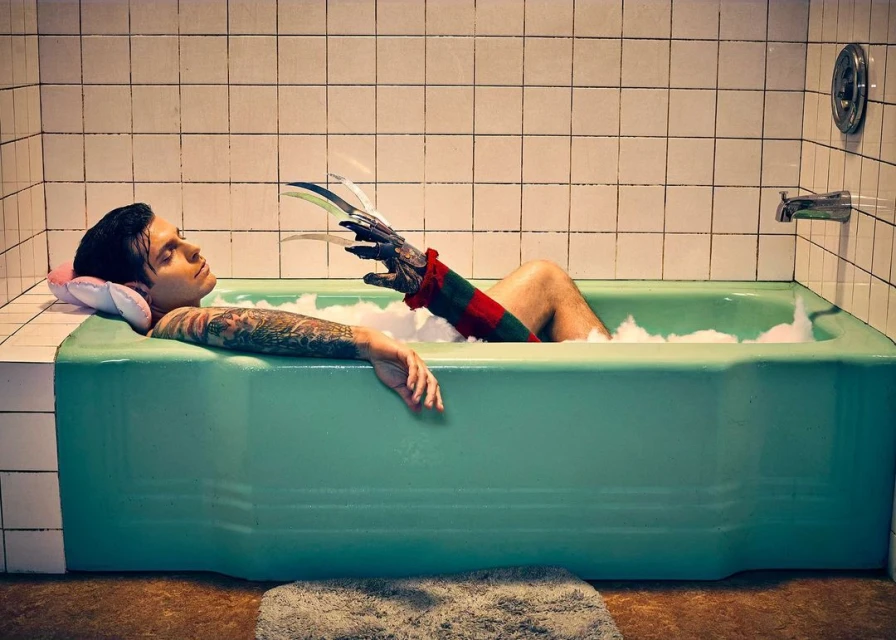 Person relaxing in a bathtub with bubble bath, an arm with long metal claws extends into the tub, tiled bathroom background.