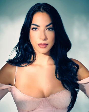 Portrait of a woman with long dark hair wearing a pale pink top against a neutral studio background
