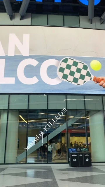 Indoor shot featuring a convention hall entrance with a large banner displaying a pickleball paddle graphic, captured in bright daylight.