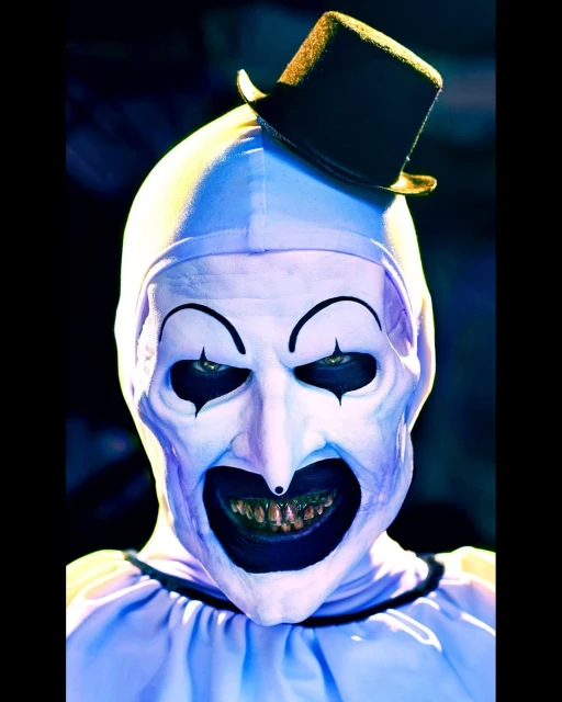 Close-up portrait of a person wearing a creepy white clown mask and black top hat with dark eyes, set against a shadowy background.