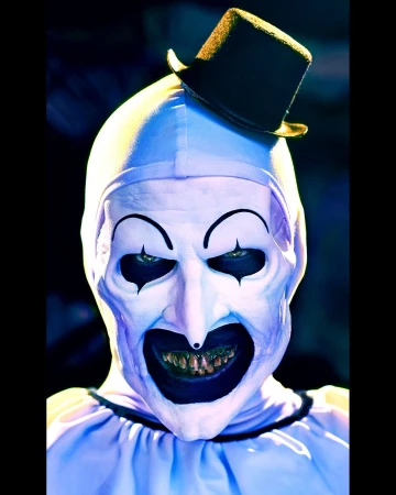 Close-up portrait of a person wearing a creepy white clown mask and black top hat with dark eyes, set against a shadowy background.