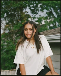 Young woman with long dark braided hair wearing a white polo shirt outdoors by foliage
