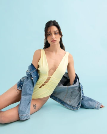 Woman in yellow swimsuit and denim jacket sitting against a light blue seamless studio backdrop by Michele Foti.