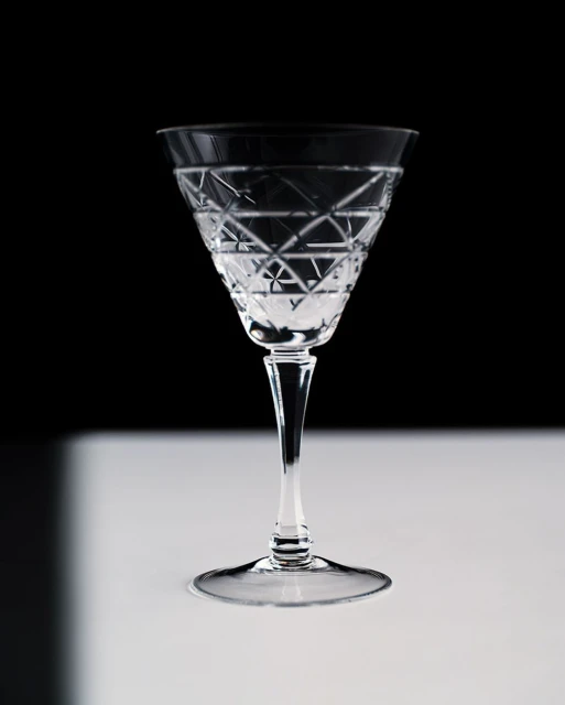 Crystal wine glass with intricate diamond pattern stands on a white surface against a stark black background in a studio setting.