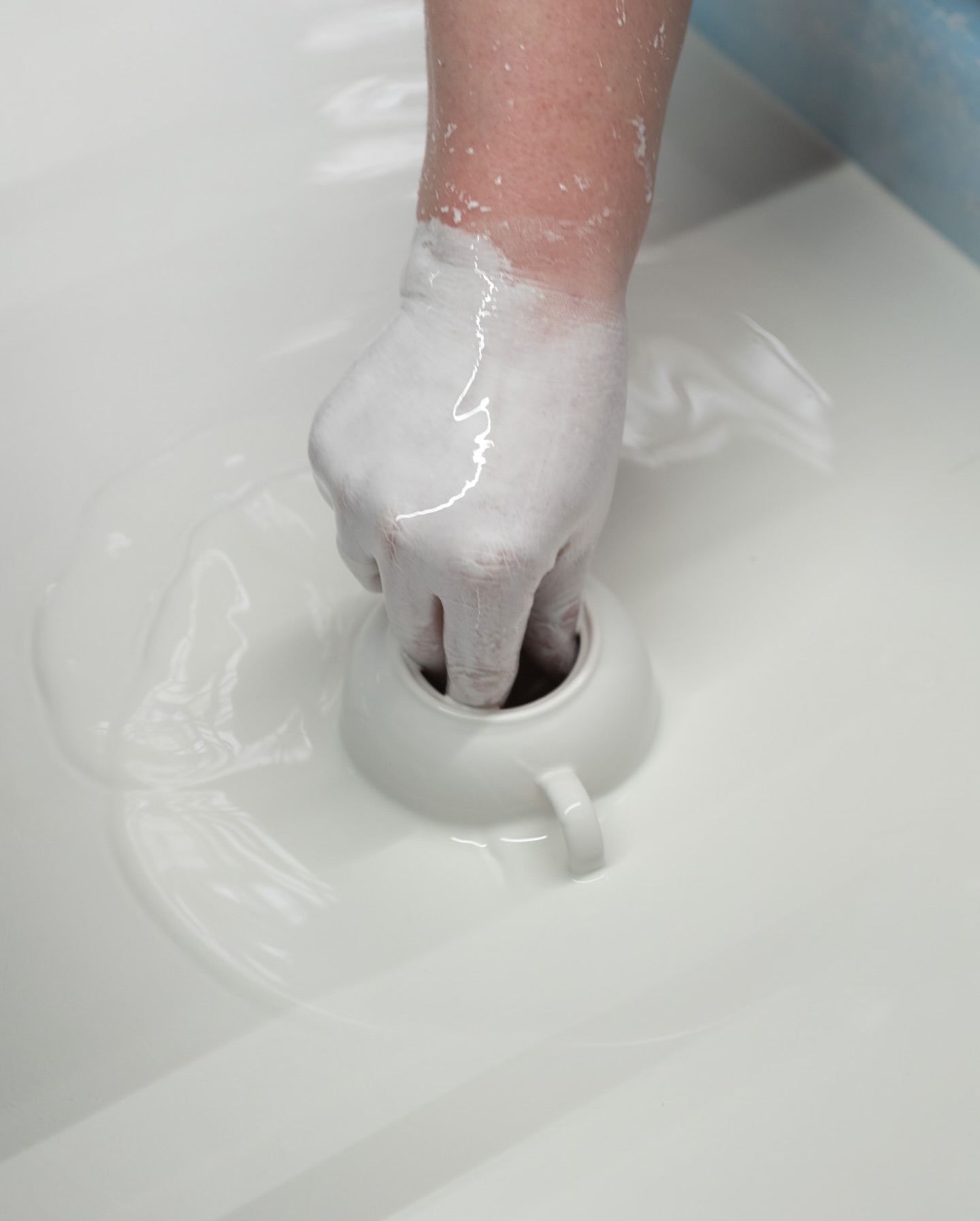 Close-up shot of a hand covered in white slip dipping a ceramic cup into a vat of slip, showcasing the pottery glazing process.