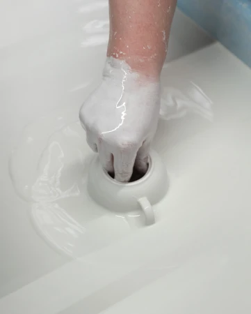 Close-up shot of a hand covered in white slip dipping a ceramic cup into a vat of slip, showcasing the pottery glazing process.