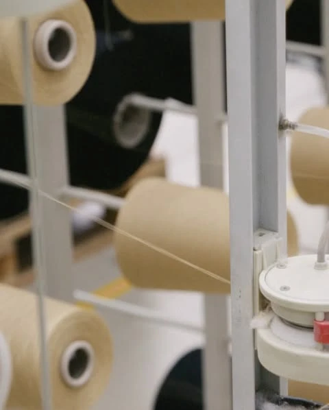 Close-up of spools of beige thread mounted on a metal rack in a factory setting, ready for textile production.