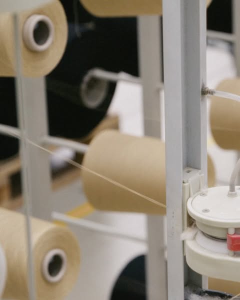Yarn spools on a rack in a textile factory with a light-toned color palette and selective focus.