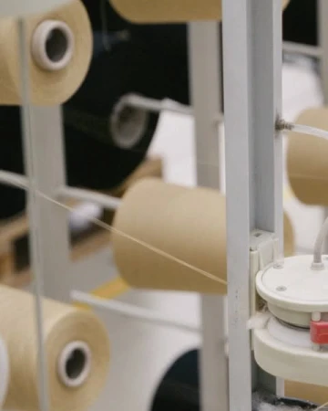 Yarn spools on a rack in a textile factory with a light-toned color palette and selective focus.