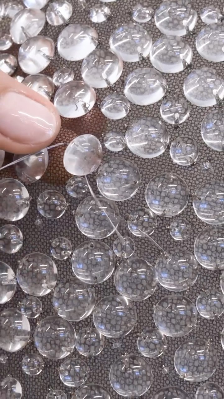 Close-up of water droplets on textured surface, finger touching a droplet. Macro photography emphasizes water's refractive properties and texture.
