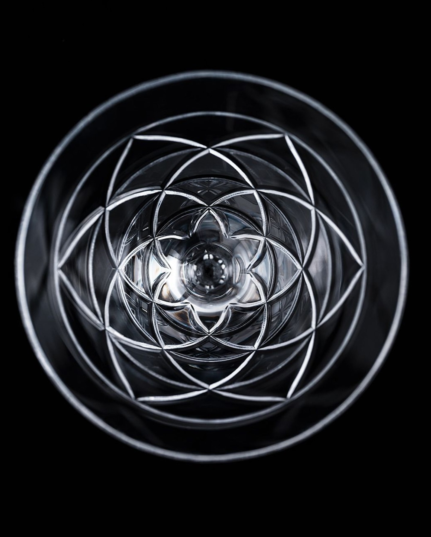 Close-up, symmetrical shot looking into a clear crystal glass with intricate starburst pattern, set against a stark black backdrop.