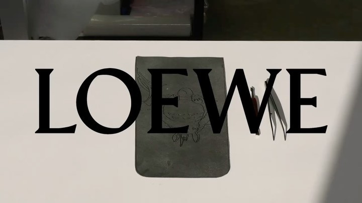 A leather wallet with a sketched animal design overlaid by the logo of the fashion brand Loewe, shot in a studio setting.