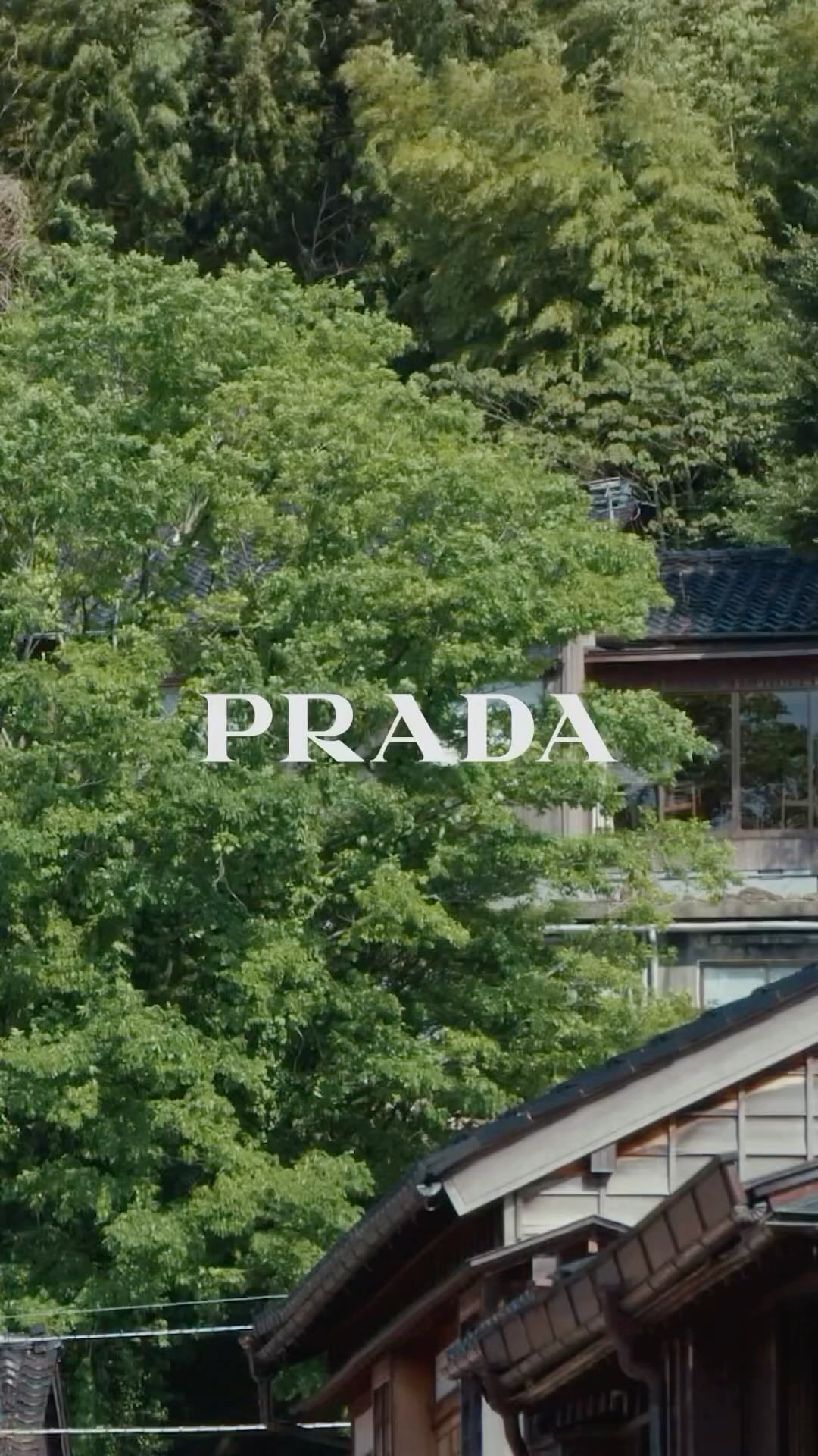 Scenic outdoor view with lush green trees, a traditional building, and the Prada logo, showcasing nature and architectural elements.