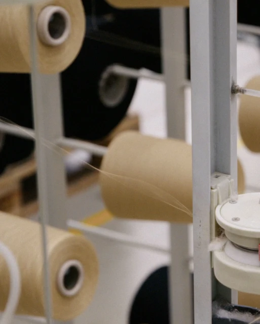 Close-up of yarn spools on a textile machine, showcasing the process of yarn production with beige and black spools. 