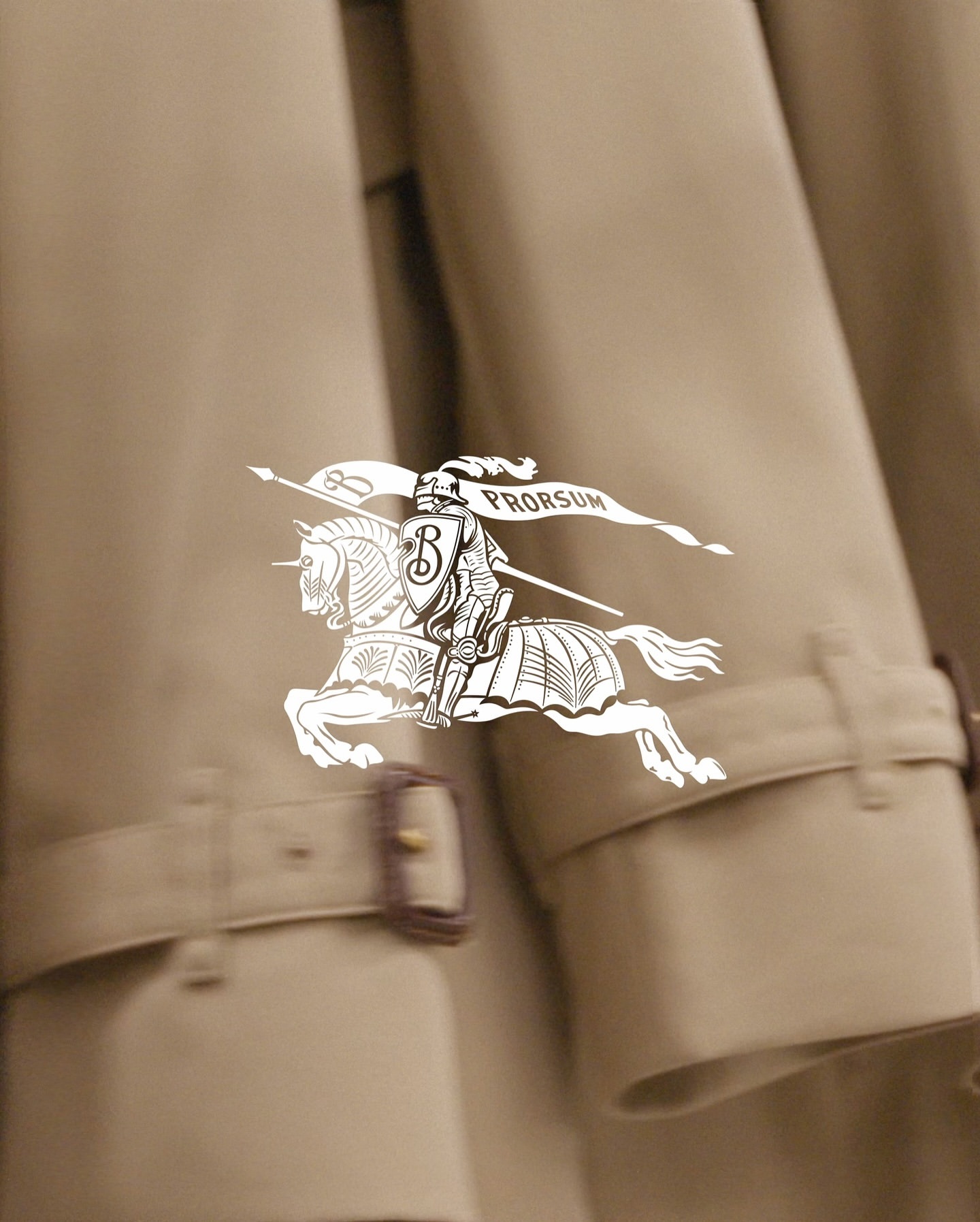 Close-up of a beige trench coat with Burberry logo featuring a knight on horseback; focus on fashion and apparel textures.
