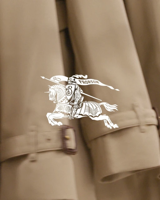 Close-up of a beige trench coat with Burberry logo featuring a knight on horseback; focus on fashion and apparel textures.