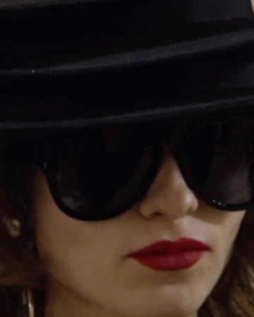 Close-up portrait of a woman wearing black sunglasses, a dark fedora hat, and bright red lipstick.
