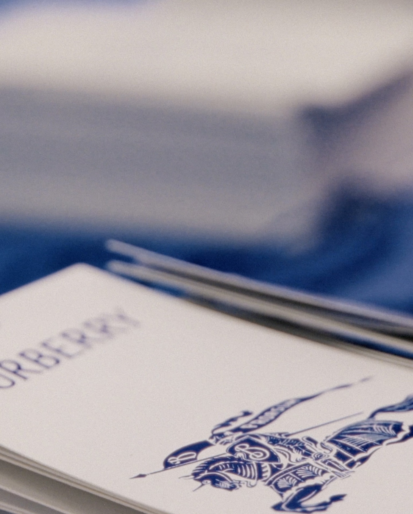 Close-up shot of white cards with blue Burberry logo and design, stacked on top of each other. Soft focus on the background.