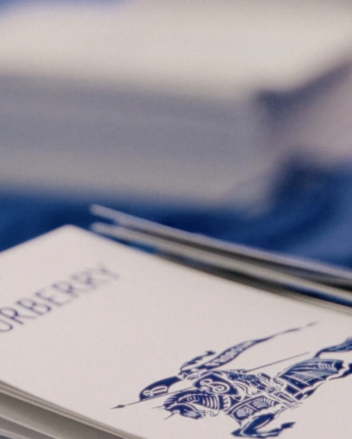 Close-up shot of white cards with blue Burberry logo and design, stacked on top of each other. Soft focus on the background.