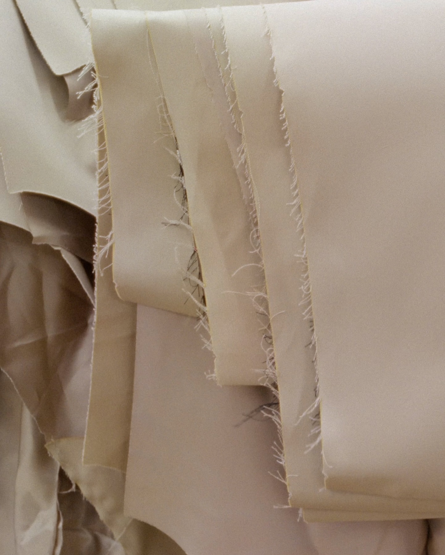 Close-up shot of beige fabric layers with frayed edges, creating a soft, textured surface. Neutral tones and subtle shadows.