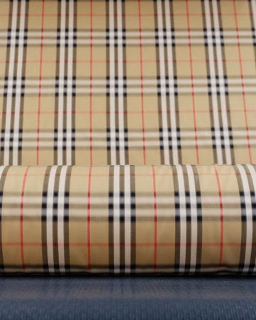 Close-up of a Burberry pattern fabric roll featuring tan, white, black, and red stripes forming a classic plaid design on a textured surface.