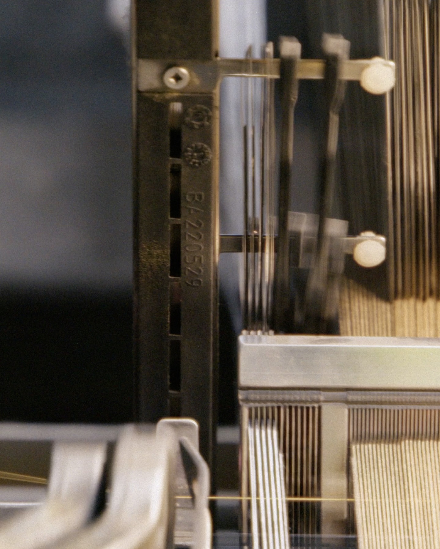 Close-up of a weaving machine's metal frame and strings, revealing its intricate mechanism and the textures of the materials.