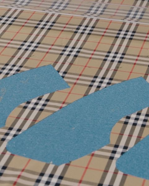 Beige plaid fabric with blue paper patterns, flat lay. Abstract sewing or textile design concept.