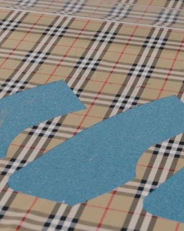 Beige plaid fabric with blue paper patterns, flat lay. Abstract sewing or textile design concept.