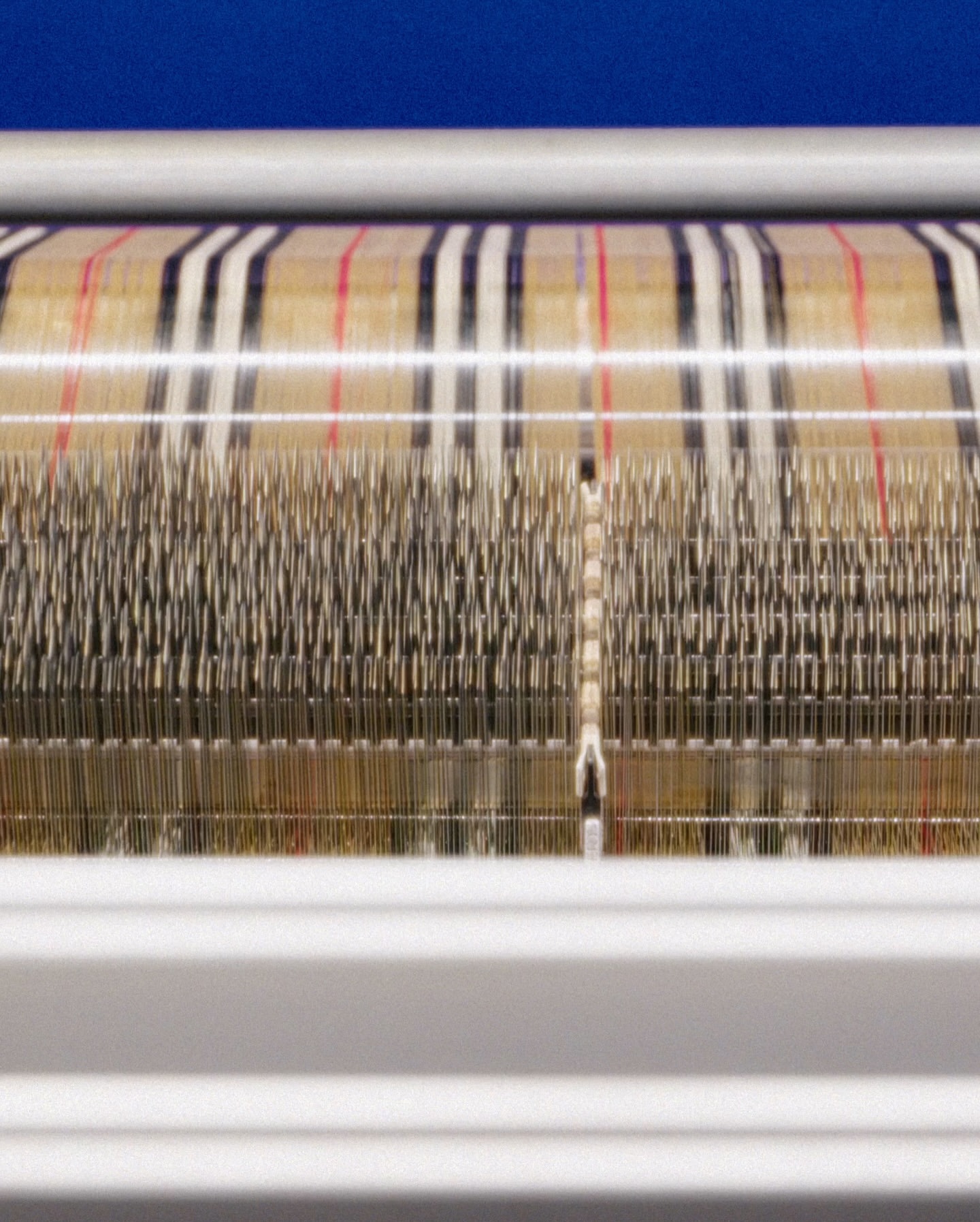 Close-up of weaving machine creating a plaid textile pattern in cream, black, and red, demonstrating textile manufacturing and design.