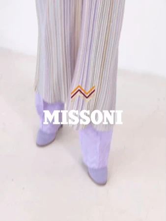 Low angle view of person wearing pleated trousers and lilac boots against a white background