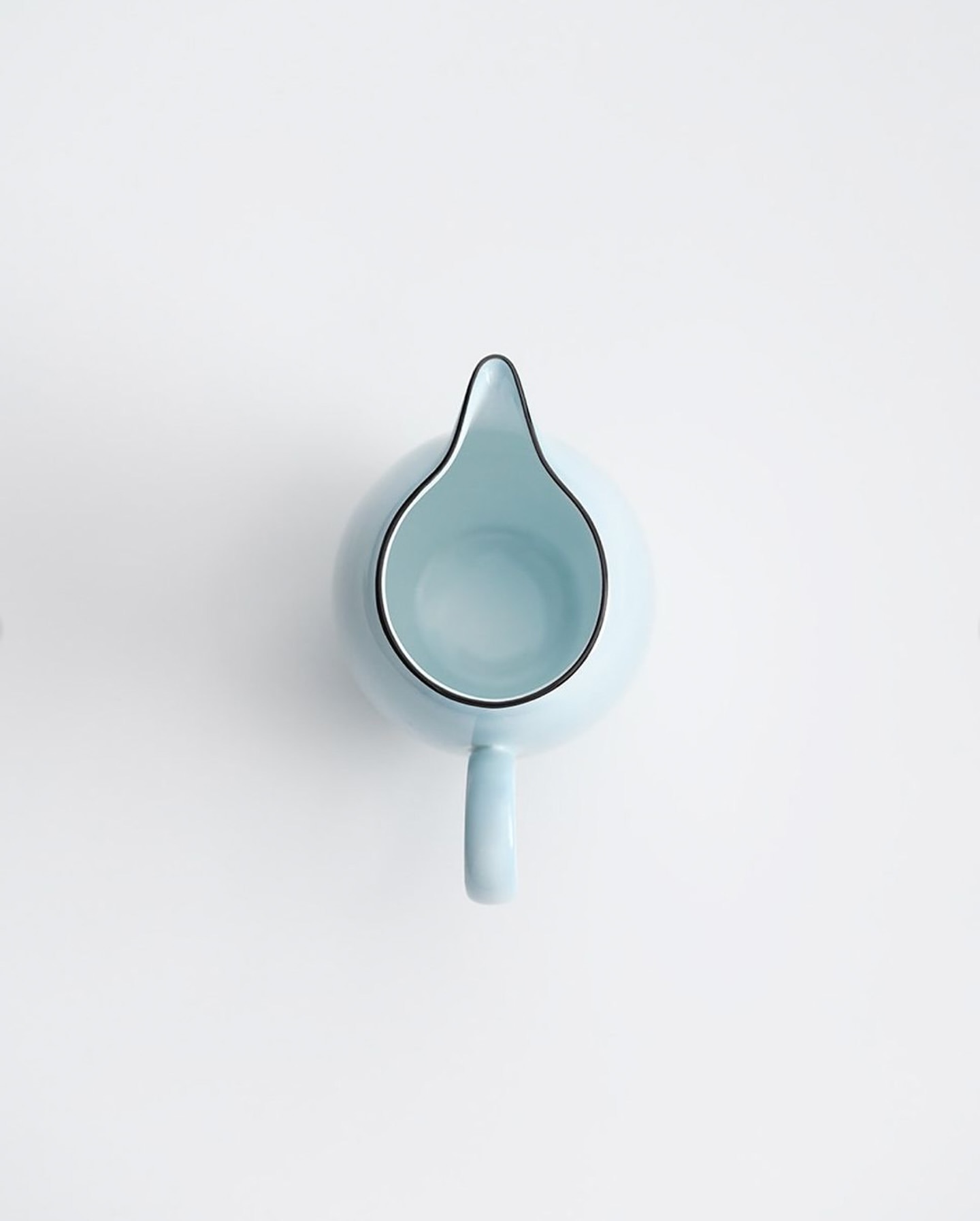 Overhead shot of a light blue ceramic milk pitcher with black trim on a white surface, showcasing its minimalist design and smooth texture.