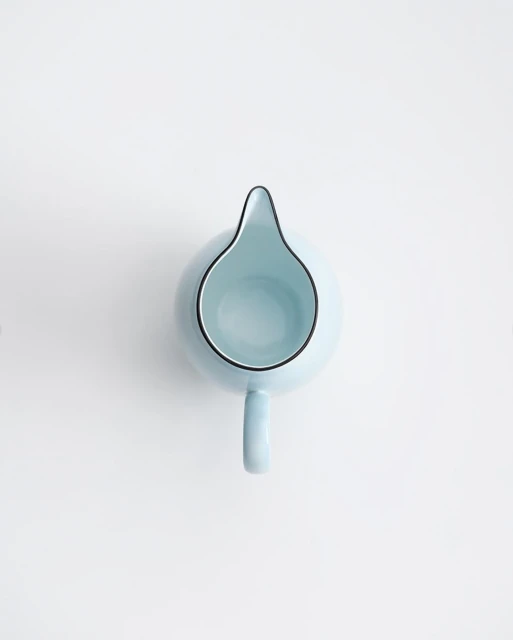 Overhead shot of a light blue ceramic milk pitcher with black trim on a white surface, showcasing its minimalist design and smooth texture.