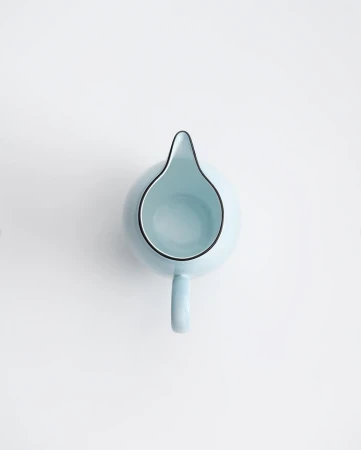 Overhead shot of a light blue ceramic milk pitcher with black trim on a white surface, showcasing its minimalist design and smooth texture.
