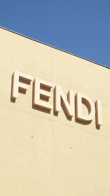 Close-up of Fendi brand signage on the exterior wall of a building under a clear blue sky, architectural shot with a vertical composition.