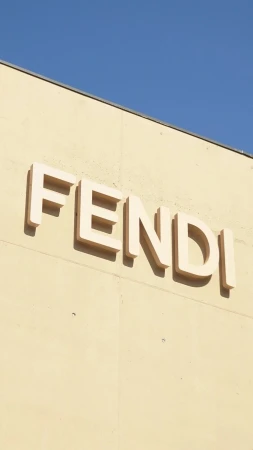 Close-up of Fendi brand signage on the exterior wall of a building under a clear blue sky, architectural shot with a vertical composition.